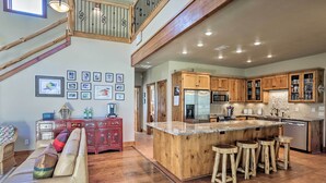 A spacious kitchen with wooden cabinets, a large island with stools, and a dining area with a sofa and a red cabinet. - Riverfront Blanco Home w/ Shaded Porch + Hot Tub (Blanco)
