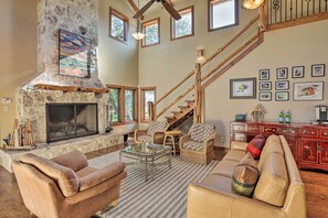 A spacious living room with a stone fireplace, wicker furniture, a staircase, and framed artwork on the walls.