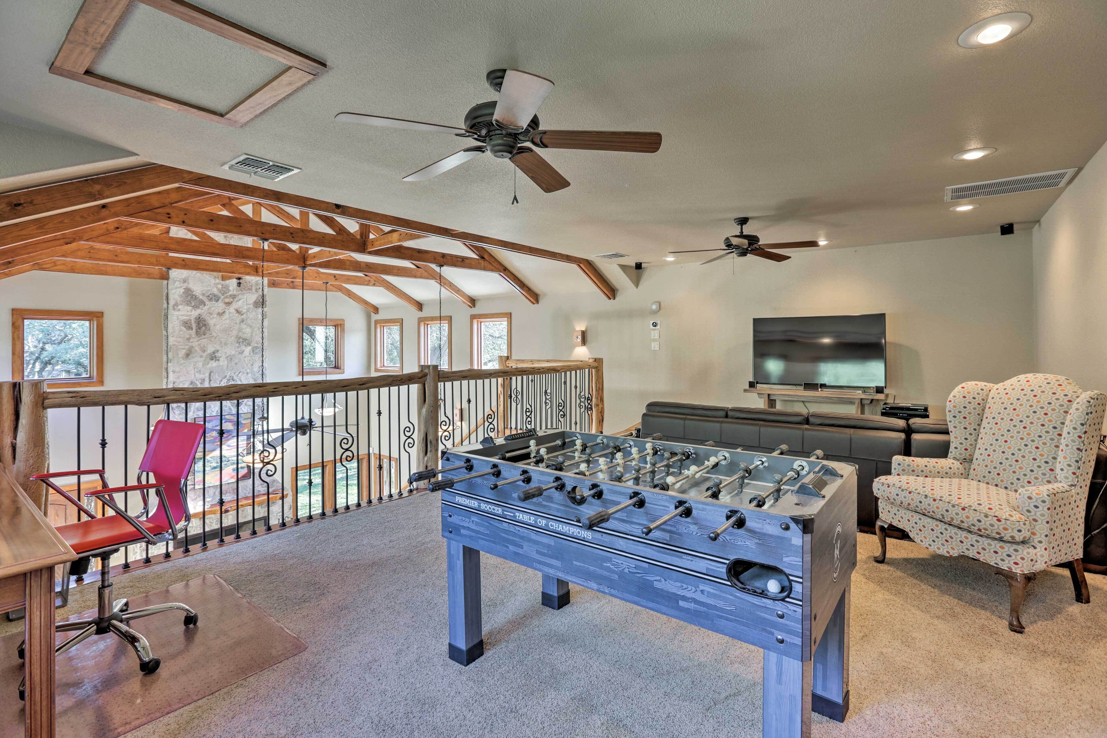 A spacious room with a foosball table, a television, and a balcony with a railing.