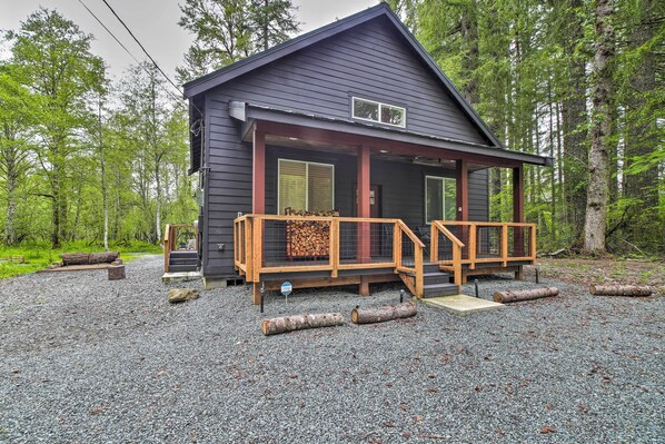 A cabin with a porch, a covered entryway, and a gravel driveway.
