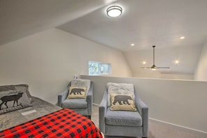 A bedroom with a bed, two armchairs, a ceiling fan, and a window.
