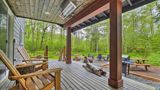 A wooden deck with outdoor seating, a grill, and a view of a forested area. - Modern Hideaway: Fire Pit, 5 Mi to Mt Rainier (Mineral)