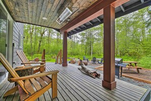 Eine Holzterrasse mit Sitzgelegenheiten, einem Grill und Blick auf eine bewaldete Landschaft.