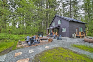 A cabin with a gravel driveway, outdoor seating, and a forest backdrop.