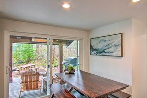 A wooden dining table with benches, a grill outside, and a painting on the wall.