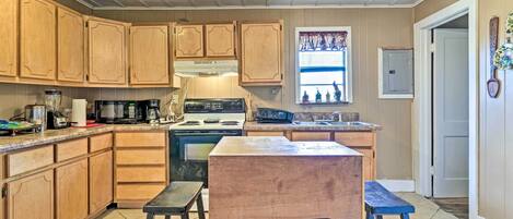 A kitchen with wooden cabinets, a stove, a microwave, and a window with decorations.