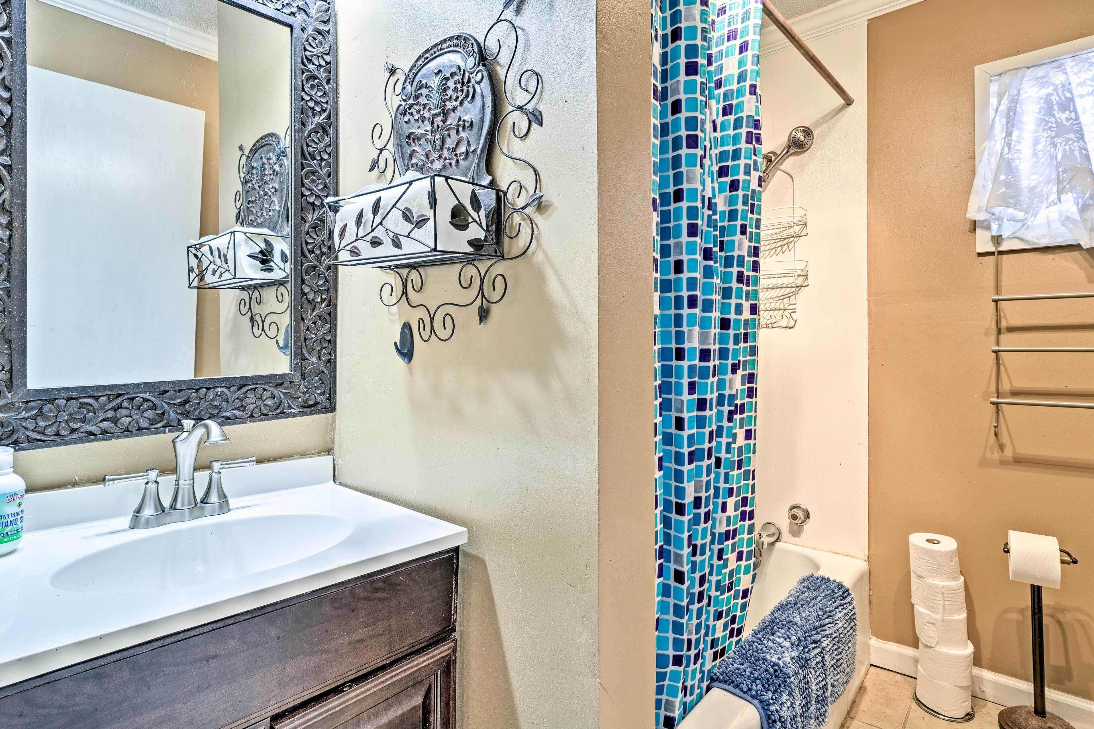 Un baño con un lavabo blanco, un espejo con detalles metálicos ornamentales, una ducha con cortina de mosaico azul y un perchero para toallas.