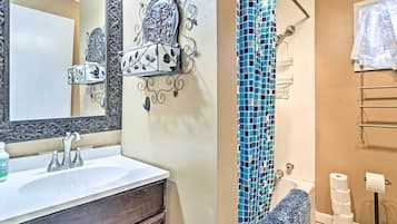 A bathroom with a white sink, a mirror with ornate metalwork, a shower with a blue mosaic curtain, and a towel rack.