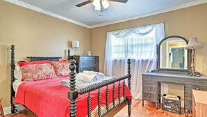Een slaapkamer met een hemelbed, een dressoir, een spiegel en een plafondventilator.