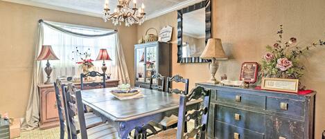 Un comedor con una mesa de madera, sillas, una araña y un aparador con objetos decorativos.