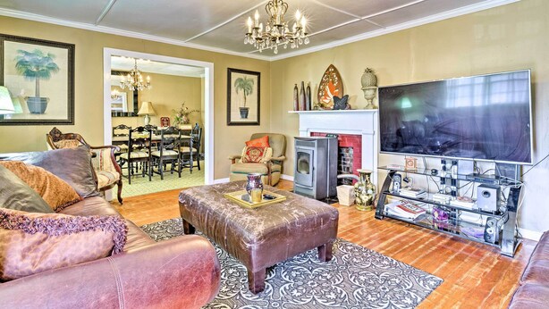 Een woonkamer met een bank, poef, kroonluchter, flatscreen televisie, open haard en een eethoek met stoelen en een tafel.