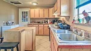 Une cuisine avec des meubles de rangement en bois, un îlot central, un évier et une fenêtre agrémentée d’objets décoratifs.