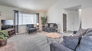 A modern living room with a flat-screen TV, grey sofas, a coffee table, and a potted plant. - Renovated Bakersfield Home w/ Private Yard! (Bakersfield)