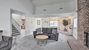 A spacious living room with a grey sofa, a round coffee table, and a brick fireplace. - Renovated Bakersfield Home w/ Private Yard! (Bakersfield)