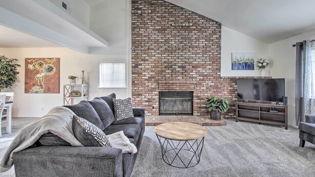 A living room with a brick fireplace, a grey sofa, a round coffee table, and a TV on a wooden stand. - Renovated Bakersfield Home w/ Private Yard! (Bakersfield)