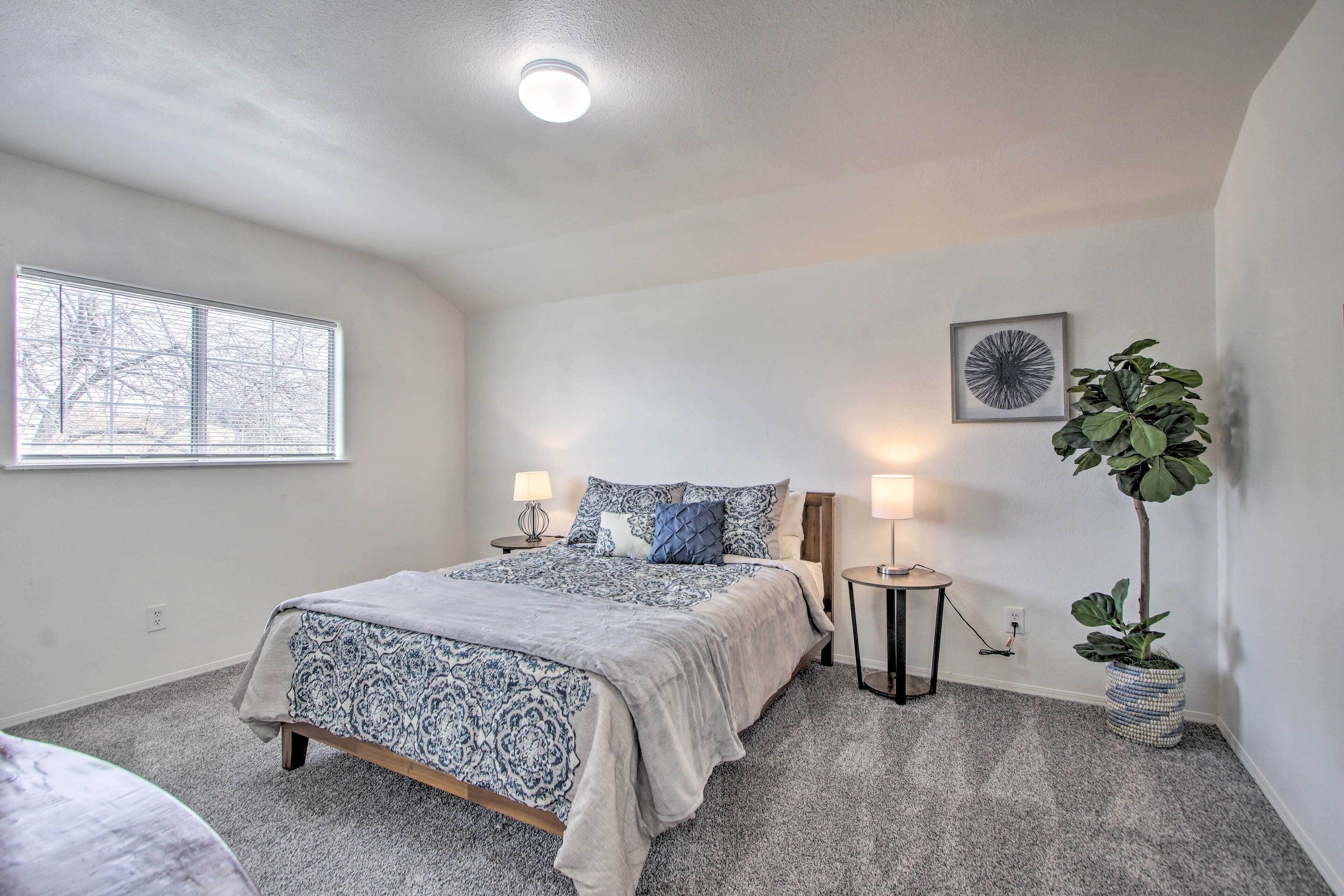 A bedroom with a bed, bedside lamps, a potted plant, and a window.