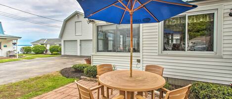 A patio with a round wooden table and chairs, a blue umbrella, and a house in the background.