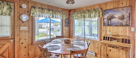 A wooden cabin interior with a round dining table, chairs, a wooden side table, and a painting of a moose.