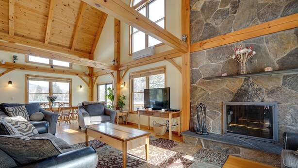 A spacious living area with a stone fireplace, wooden beams, and a television. - Secluded Vermont Retreat: Outdoor Pool & Deck (West Wardsboro)