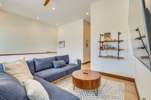 A modern living room with a grey sectional sofa, a wooden coffee table, and a patterned rug. There are bookshelves with various items and a painting on the wall. - Modern Fraser Townhome w/ Private Hot Tub & Decks! (Fraser)
