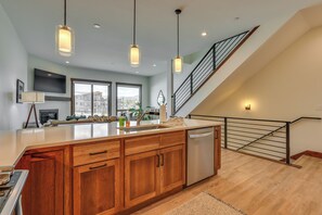 A spacious kitchen with wooden cabinets, a large island, stainless steel appliances, pendant lighting, and a view of the city through large windows. - Modern Fraser Townhome w/ Private Hot Tub & Decks! (Fraser)