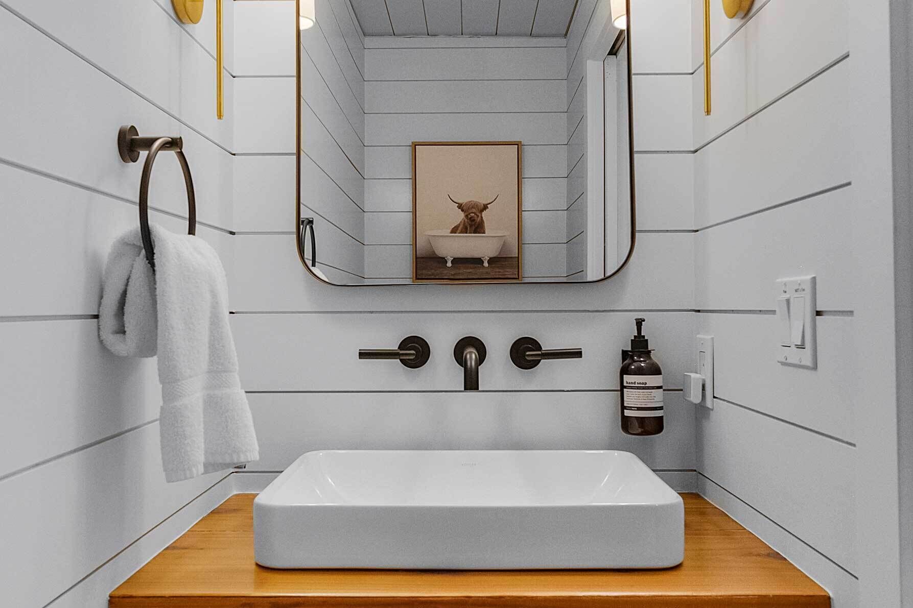 Een badkamer met een witte wastafel, een handdoekhouder, een handzeepdispenser en een afbeelding van een stier in een lijst aan de muur.