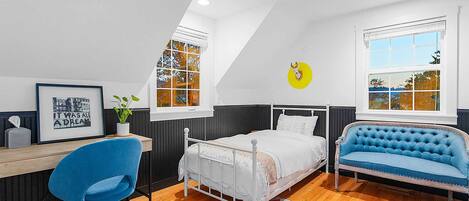 A bedroom with a bed, a desk, a chair, a blue sofa, and two windows.