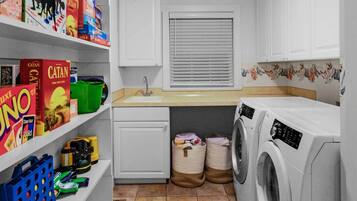 A laundry room with a washing machine, dryer, sink, and shelves with cleaning supplies.