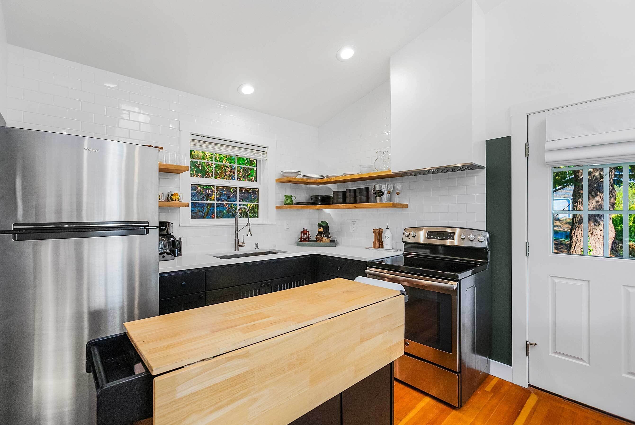 Una cocina moderna con un refrigerador de acero inoxidable, una encimera de madera, un horno integrado y un ventanal con vistas a árboles.