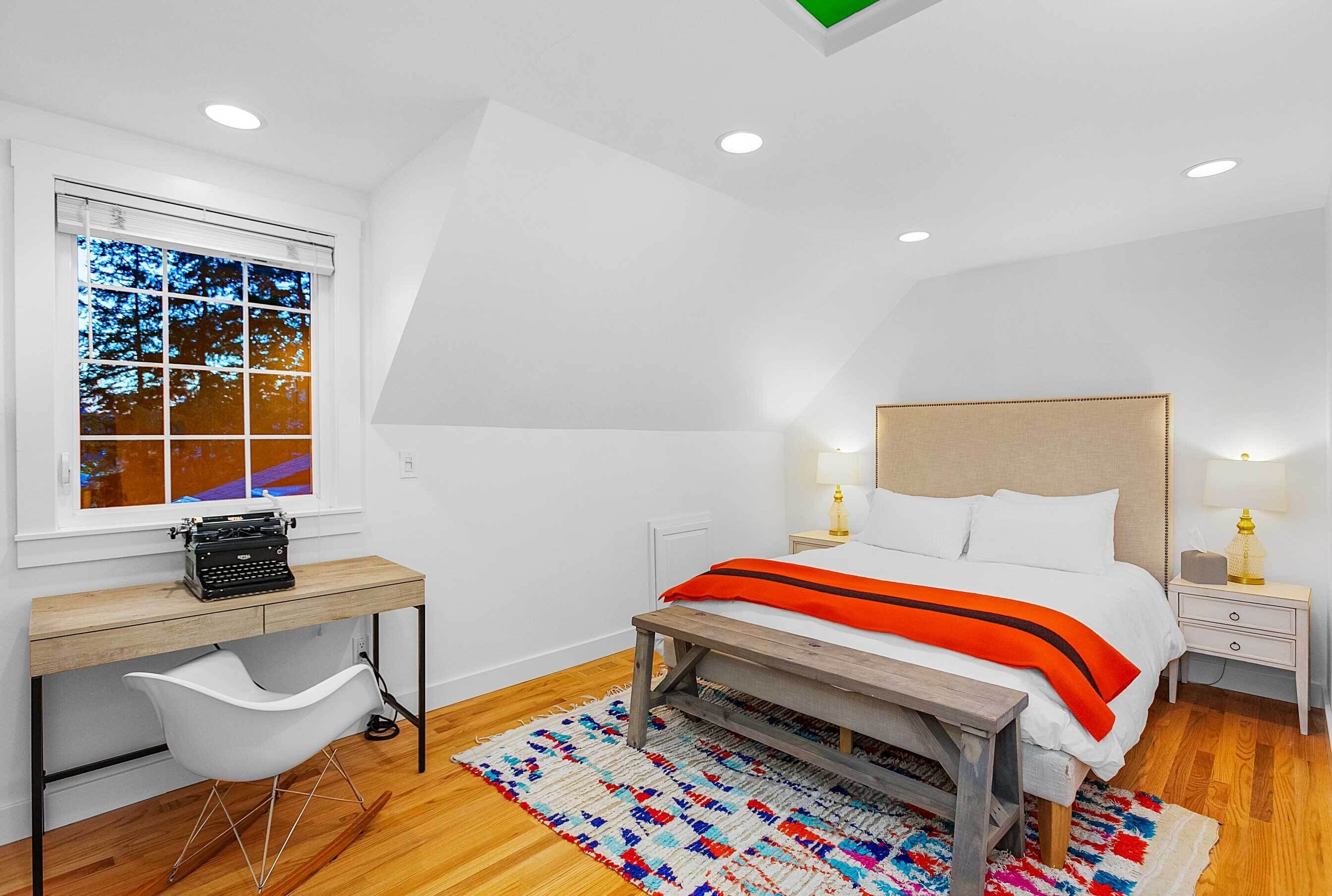 Un dormitorio con cama, mesitas de noche, escritorio, silla y ventana con persianas.