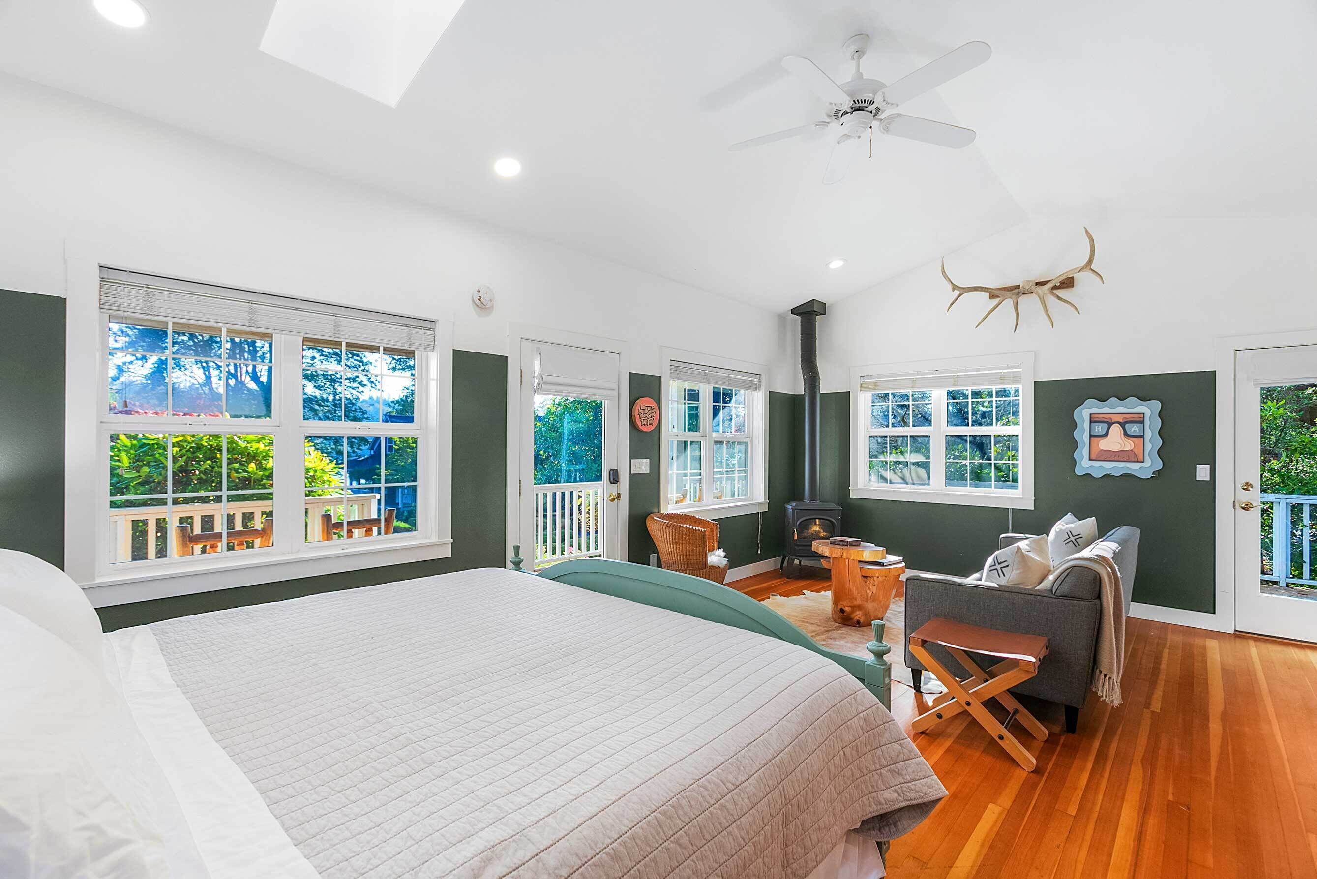 A bedroom with a bed, a seating area with a chair and a table, a fireplace, and large windows.