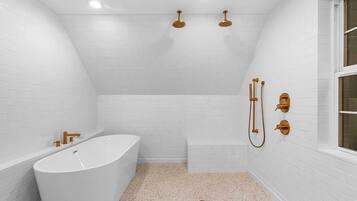 A modern bathroom with a freestanding bathtub, a shower area, and a window.