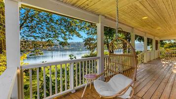A wooden deck with a hanging chair and a view of a lake.
