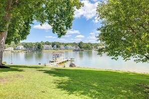 A lakeside view with a dock, grassy area, and buildings in the background. - Couples Smith Mtn Lake Getaway w/ Private Beach (Huddleston)
