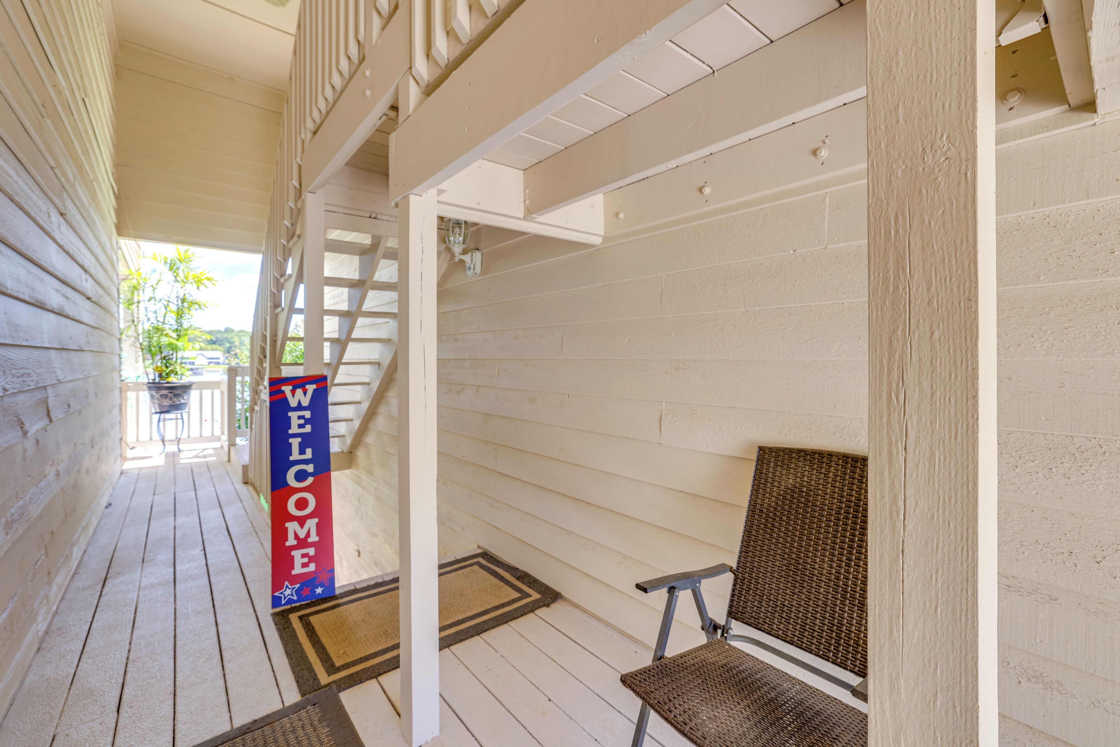 A wooden porch with a 'WELCOME' sign, a chair, and a staircase leading to an upper level.