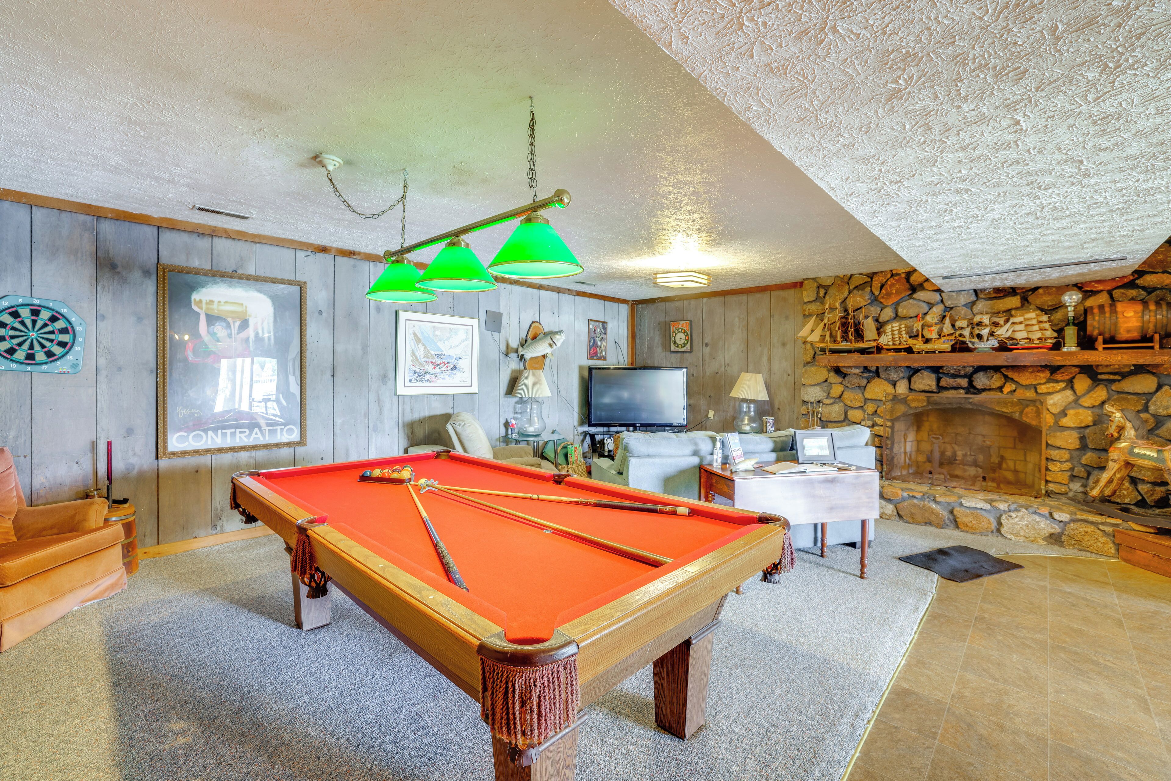 A pool table in a room with a stone fireplace, a television, and various decorations.