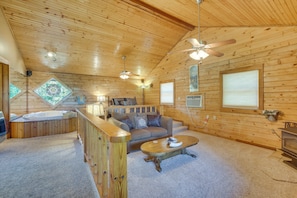 A cozy cabin interior with a wooden ceiling, a sofa, a coffee table, a fireplace, and a large window. - Studio w/ Best Mtn Views, 1 Mi to Thorncrown Chape (Eureka Springs)