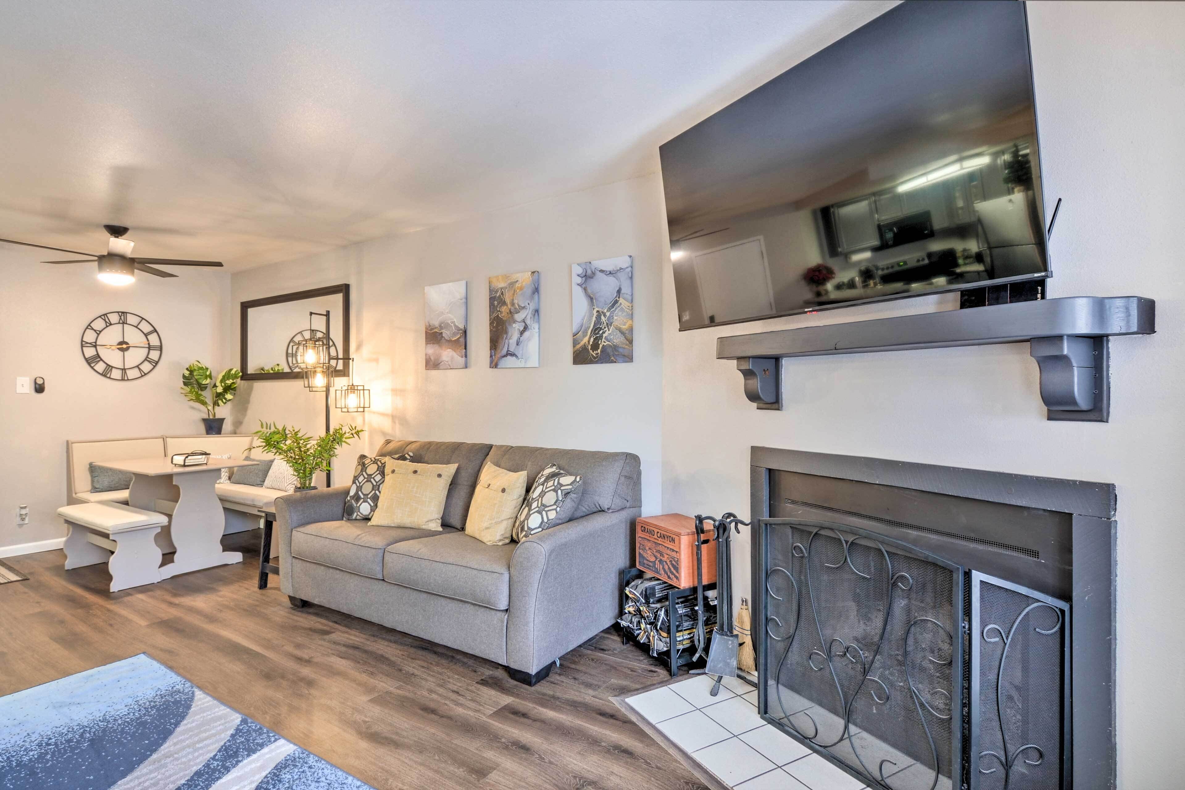 A modern living room with a grey sofa, a dining table, a ceiling fan, and a fireplace.