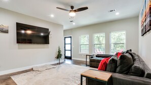 A living room with a flat-screen TV, a ceiling fan, a large window, and a dark-colored sofa. - 1 Mi to Boating & Beaches: Lake Texoma Getaway (Pottsboro)