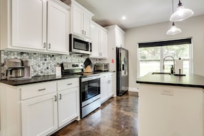 A modern kitchen with white cabinets, a stainless steel refrigerator, a microwave, a coffee maker, and a large window.