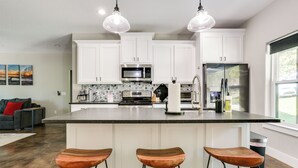A kitchen with white cabinets, a stainless steel refrigerator, a microwave, and a large island with three wooden stools. - 1 Mi to Boating & Beaches: Lake Texoma Getaway (Pottsboro)