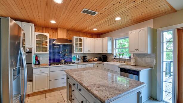 A modern kitchen with wooden ceiling, white cabinets, granite countertops, and a large island. - Sunny Lakefront Family Paradise w/ Deck & 2 Kayaks (Granbury)