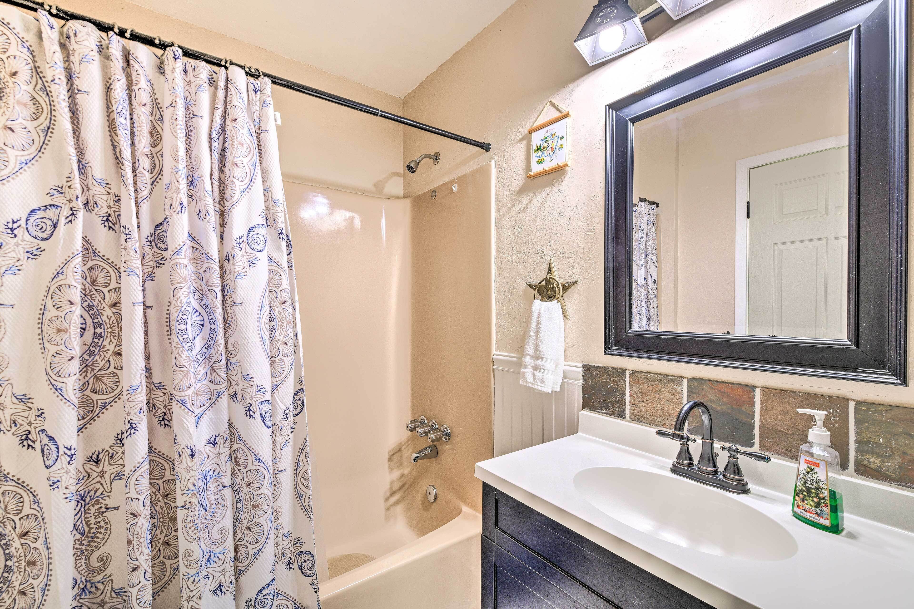 Une salle de bain avec un rideau de douche, une baignoire, un lavabo avec un miroir et un distributeur de savon.