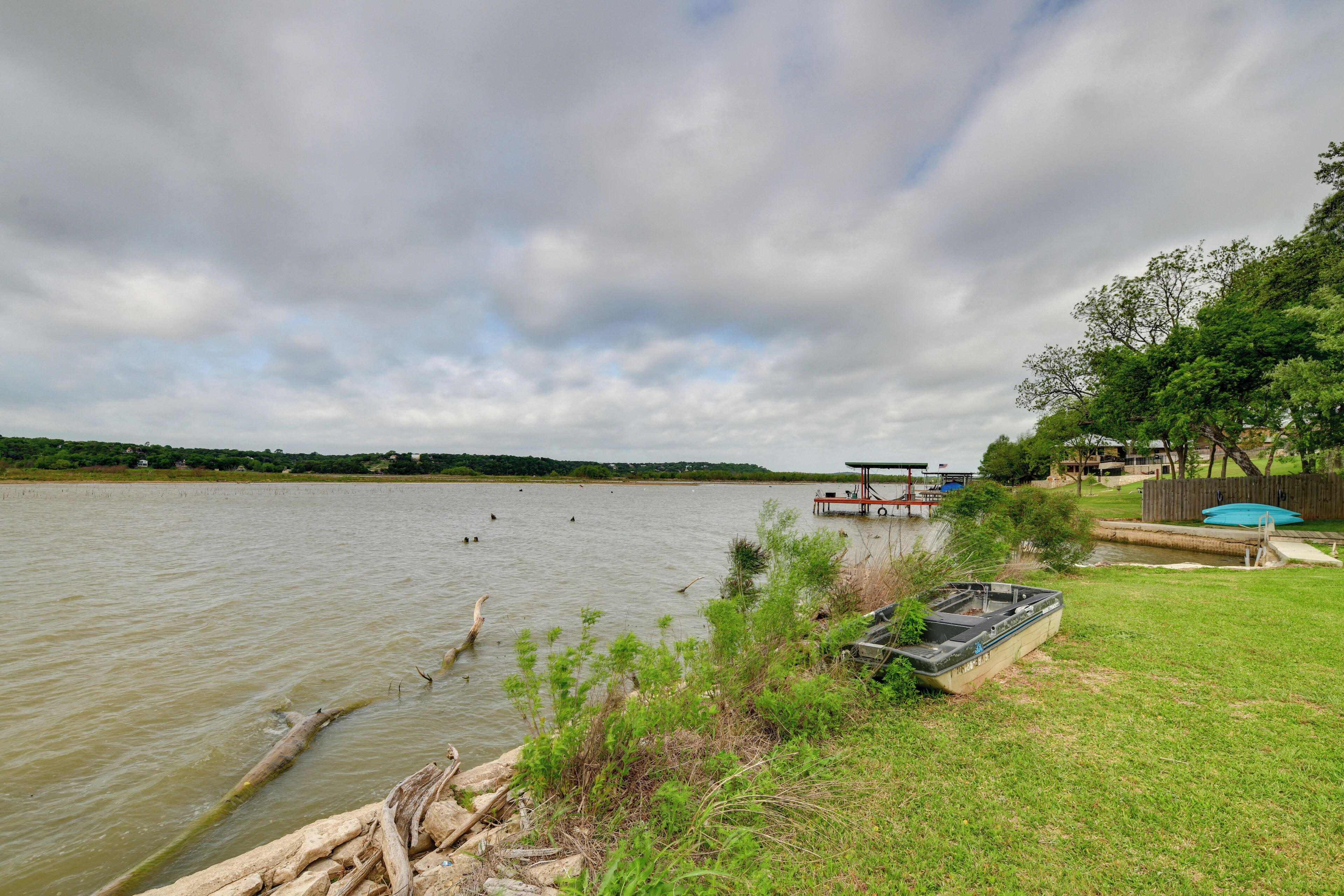 A lakeside view with a dock, a boat, and a grassy area with a wooden fence.