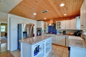 A modern kitchen with wooden ceiling, white cabinets, stainless steel appliances, and a granite countertop.