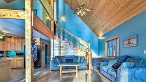 A spacious living area with a wooden staircase, a blue wall, and a kitchen in the background. - Waterfront Saginaw Bay Retreat w/ Grill & Yard! (Fairgrove)