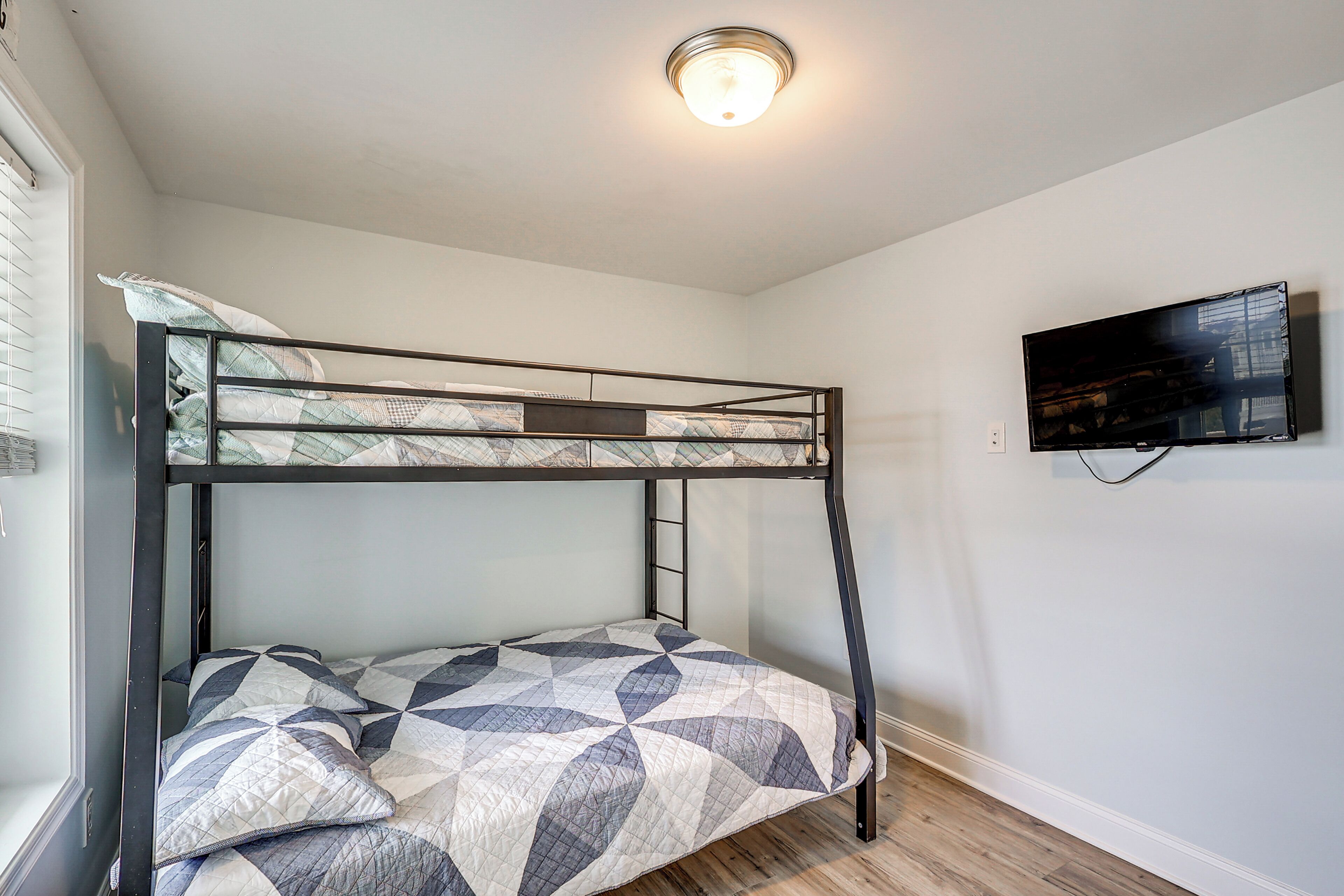 Een stapelbed met een bedspread met een geometrisch patroon, een plafondlamp en een flatscreen-televisie aan de muur.
