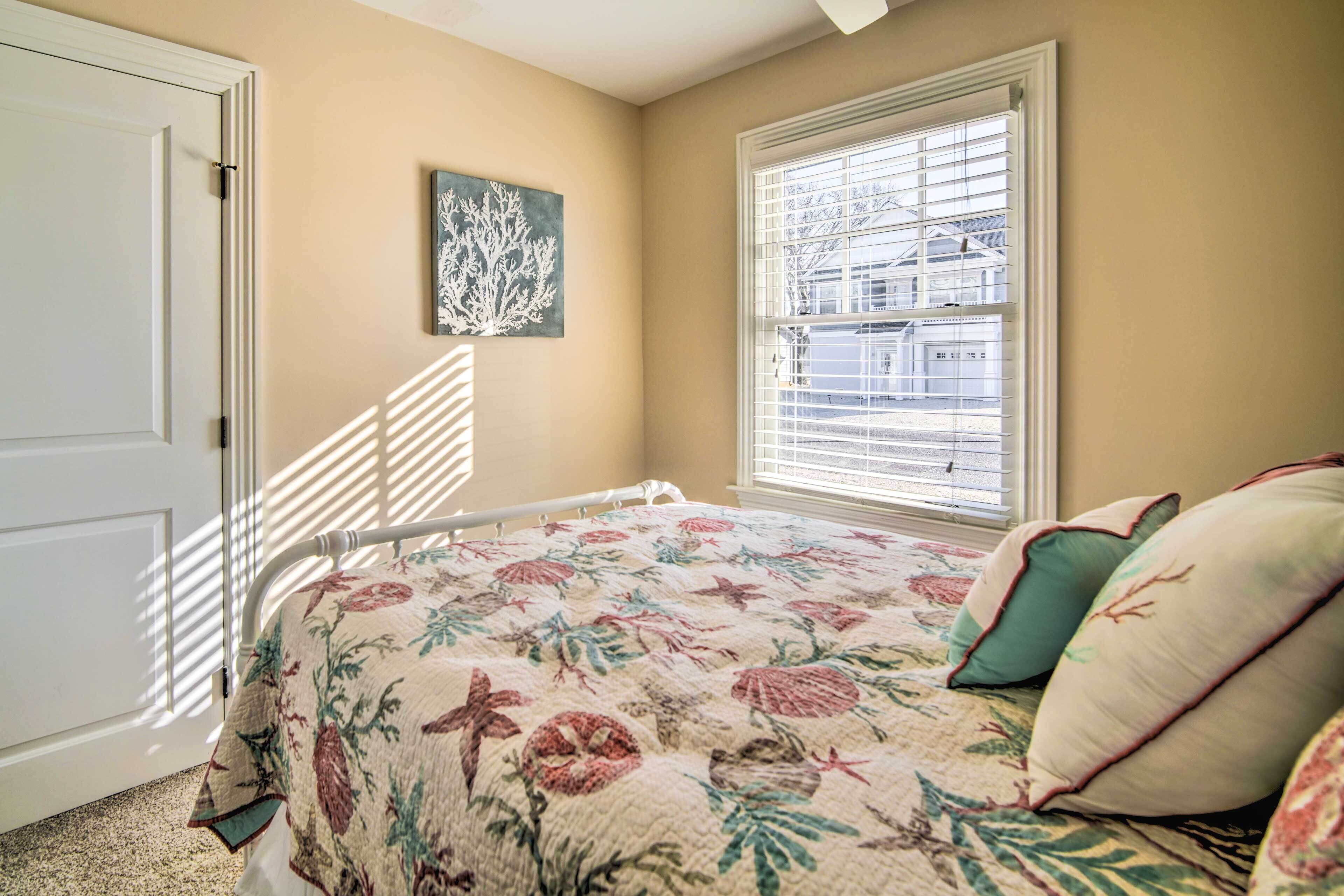 A bedroom with a bed, a window with blinds, a door, and a wall-mounted artwork.