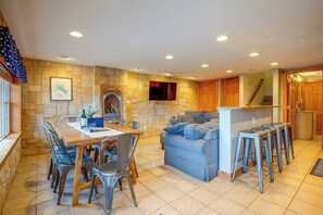 A spacious living area with a stone wall, a fireplace, a dining table with chairs, a sofa, and a kitchen area with wooden cabinets and a countertop. - Laconia Home w/ Beach - 1/2 Mi to Weirs Beach (Laconia)