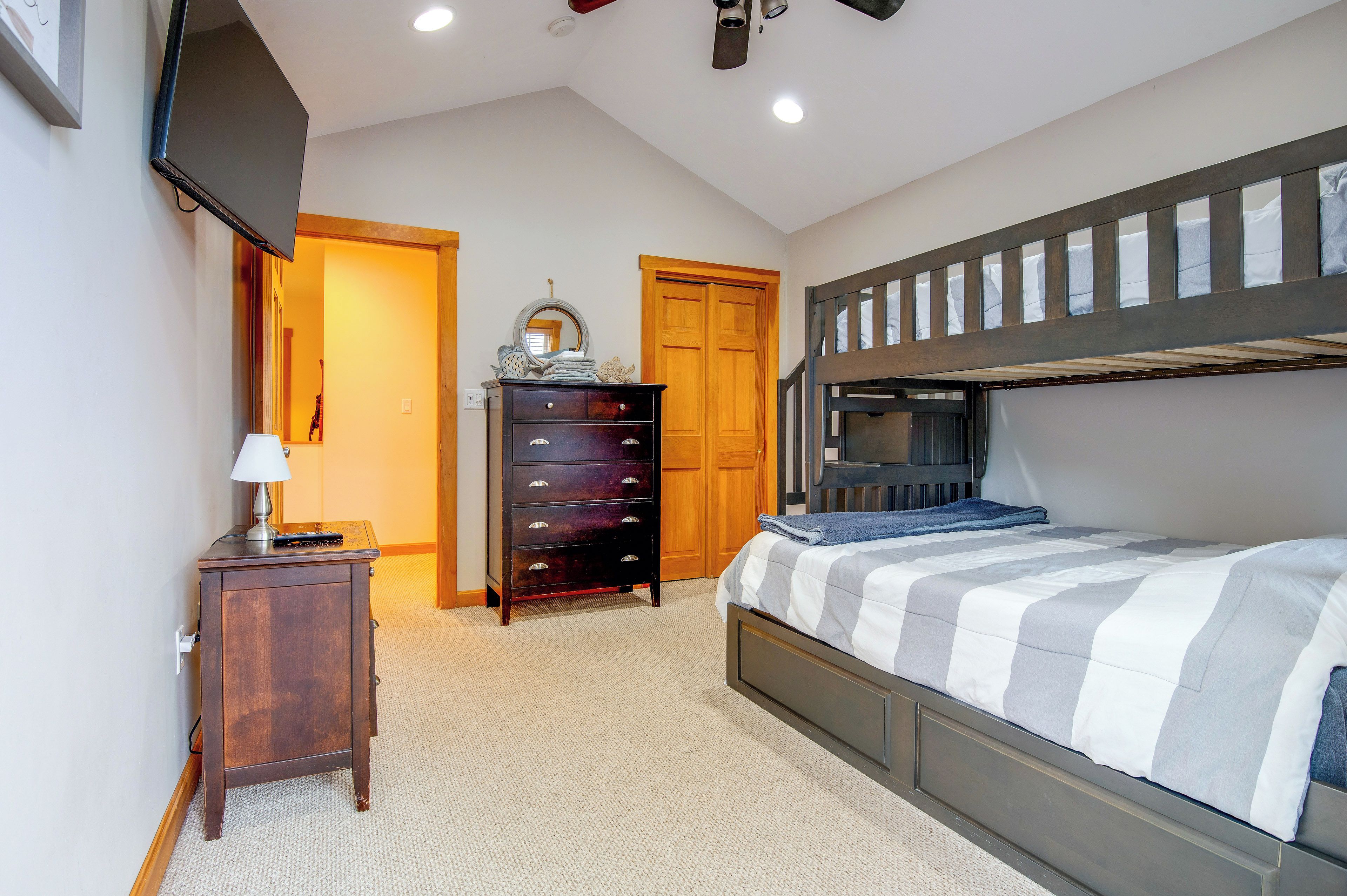 A bedroom with a bunk bed, a dresser, a lamp, and a door leading to another room.